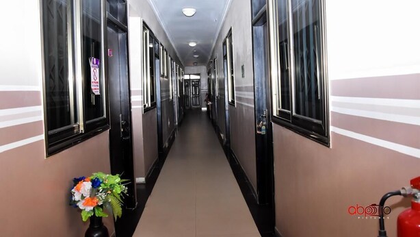 A hotel hallway with doors on both sides, a fire extinguisher on the right, and a flower arrangement on the left. - Dikab Hotel (Accra)
