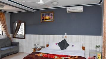 A hotel room with a bed, a sofa, a nightstand, a mirror, an air conditioning unit, and a window with curtains.