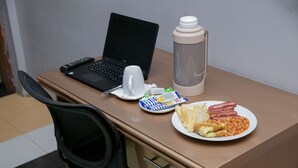 A laptop, a thermos, a plate with food, and a cup on a desk. - Dikab Hotel (Accra)