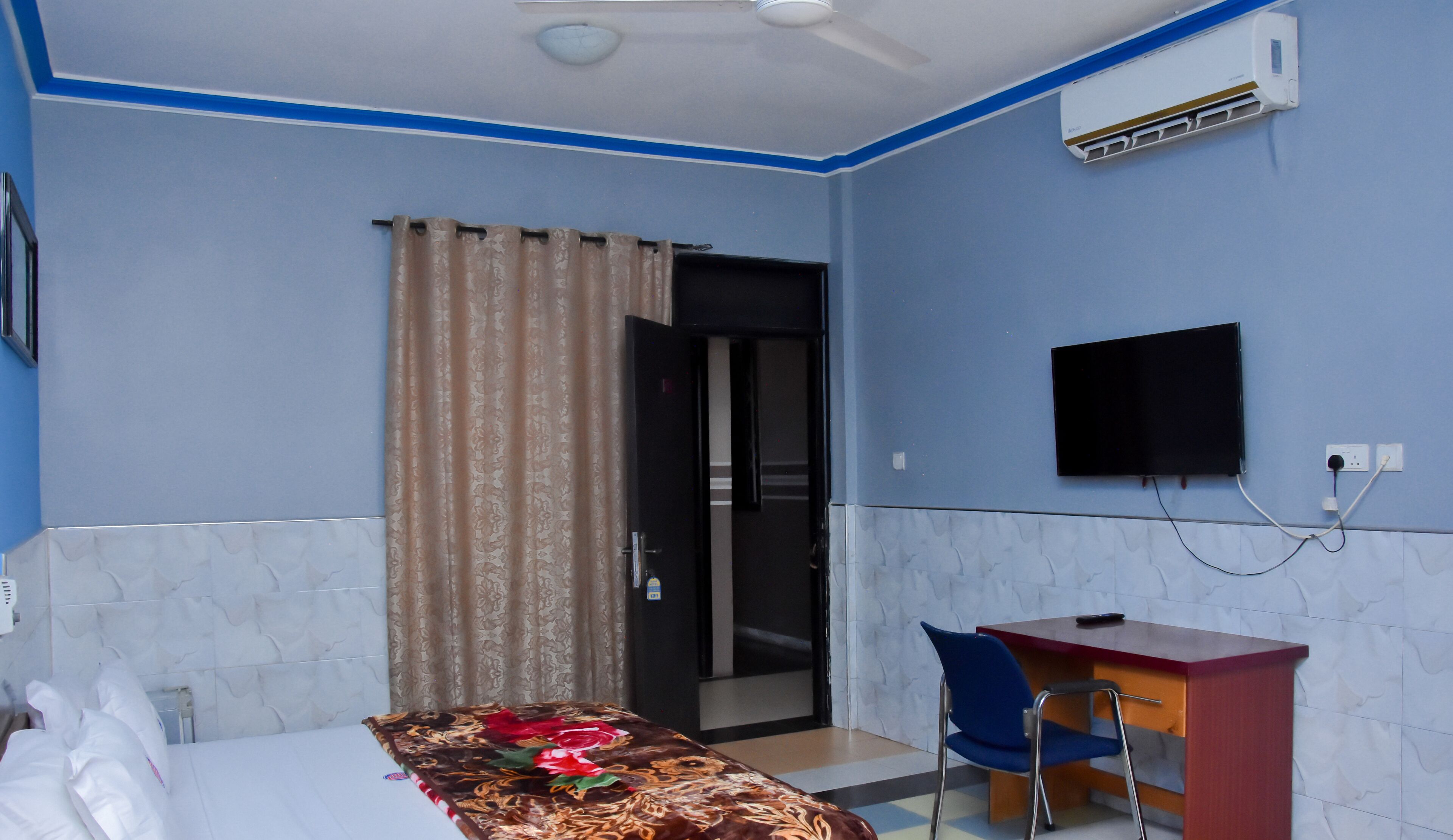 A hotel room with a bed, a desk, a chair, a television, and an air conditioning unit.