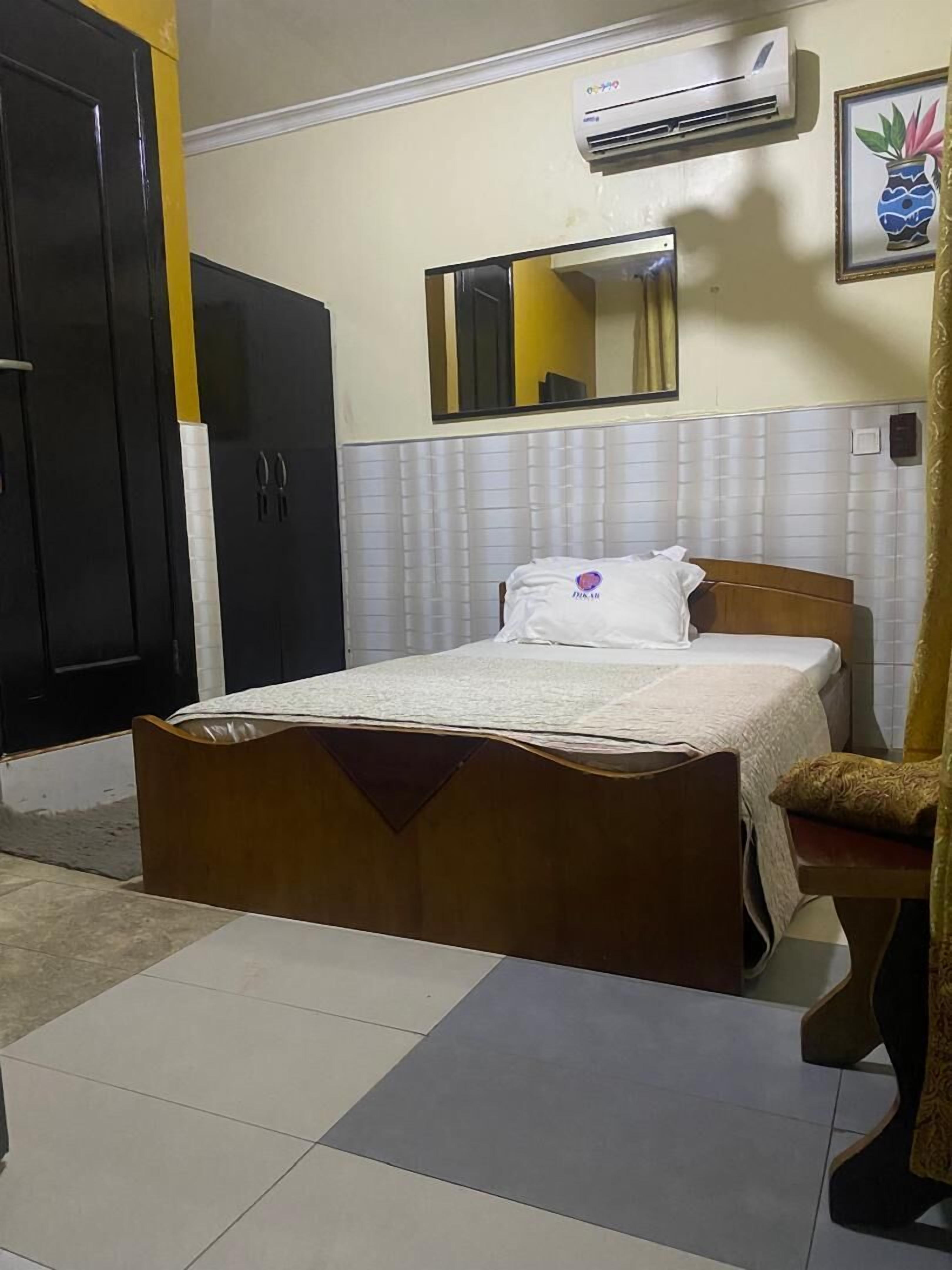 Une chambre à coucher comprenant un lit, une armoire, un appareil de climatisation, un miroir et un tableau encadré accroché au mur.