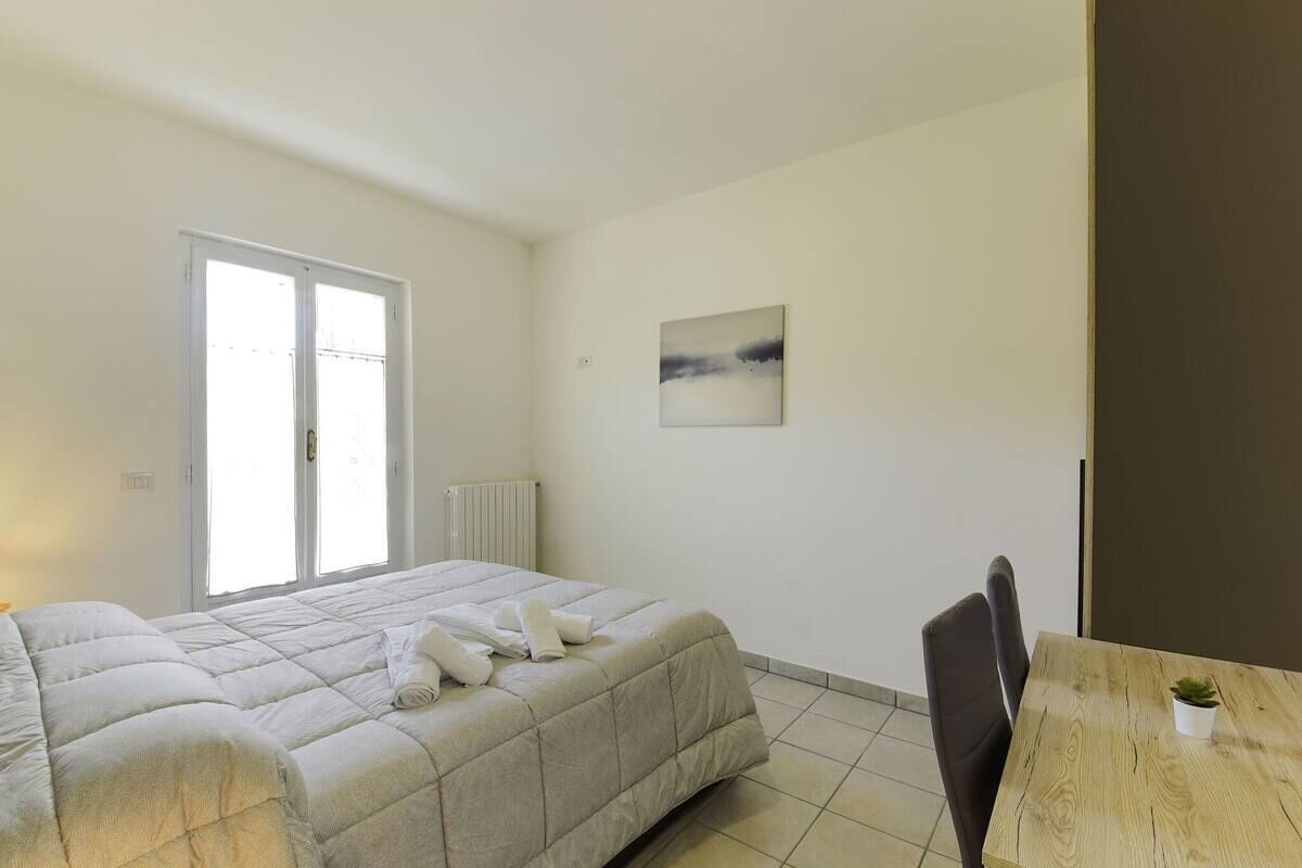 Un dormitorio con cama, una silla, una mesa y un ventanal.
