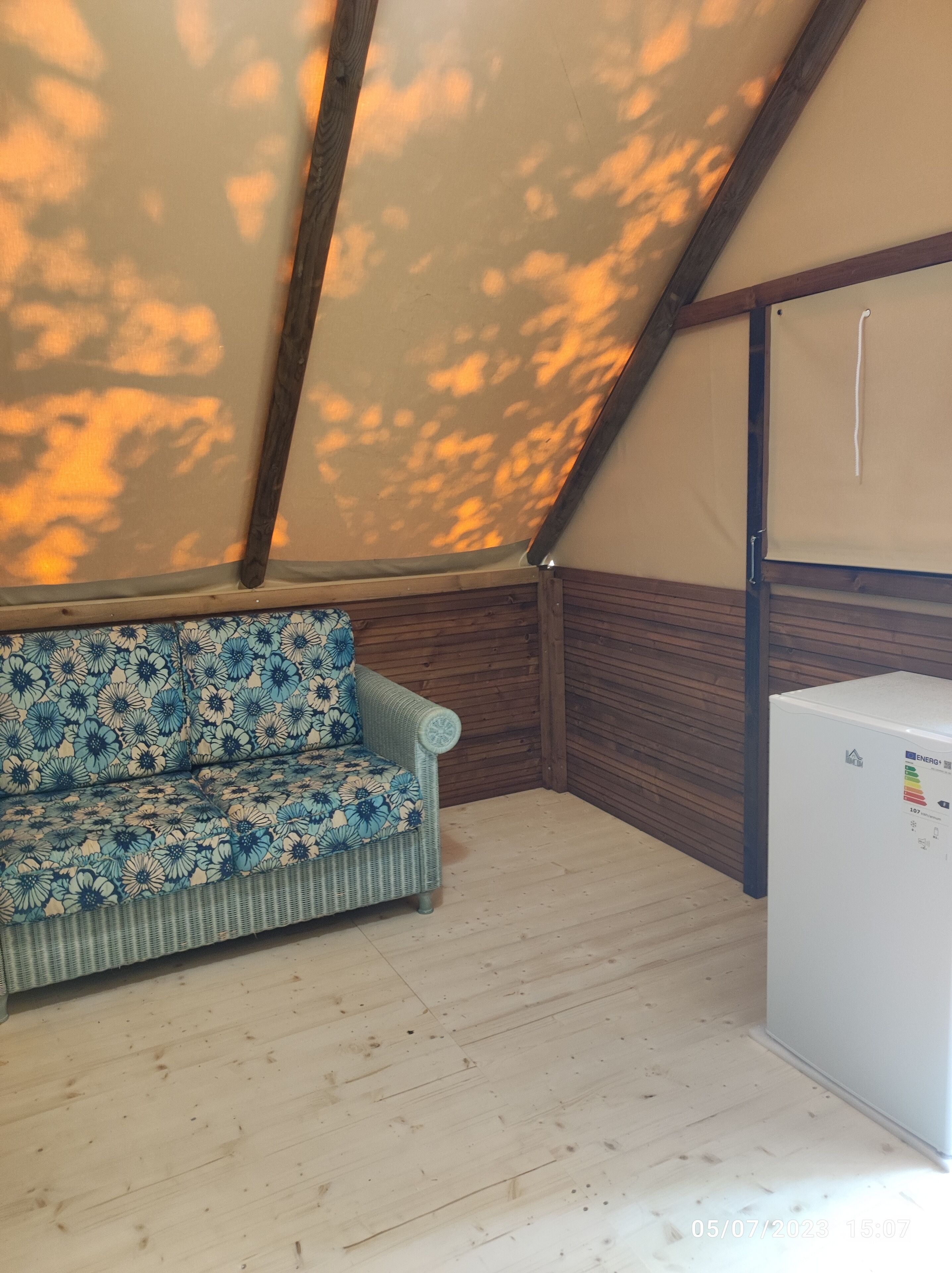 Ein Zimmer mit Holzboden, einer floralen Couch und einem weißen Kühlschrank.