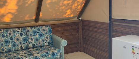 A room with a wooden ceiling, a sofa with a floral pattern, and a white refrigerator.