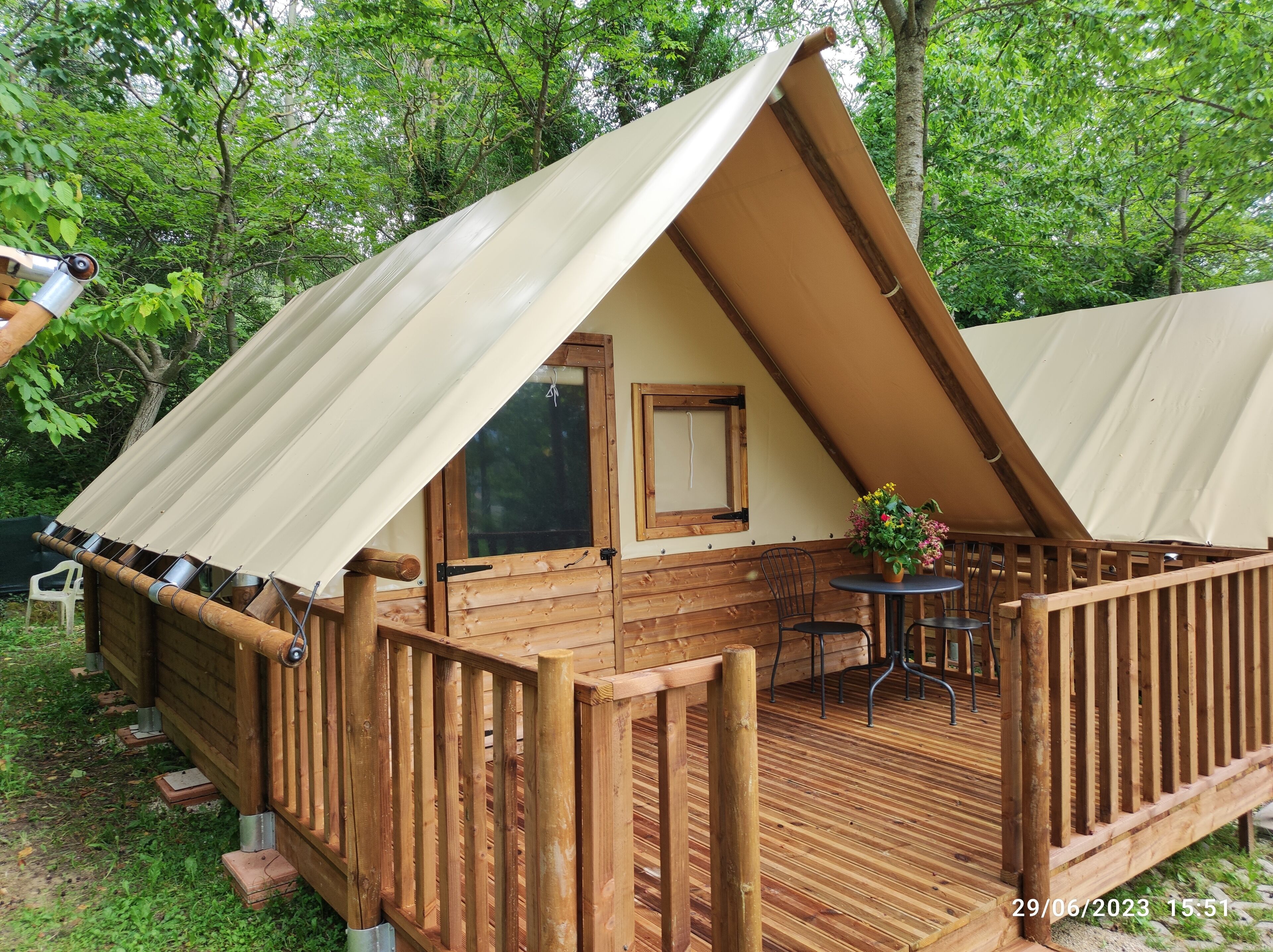 A wooden cabin with a sloped roof, a wooden deck, and a small table with chairs.