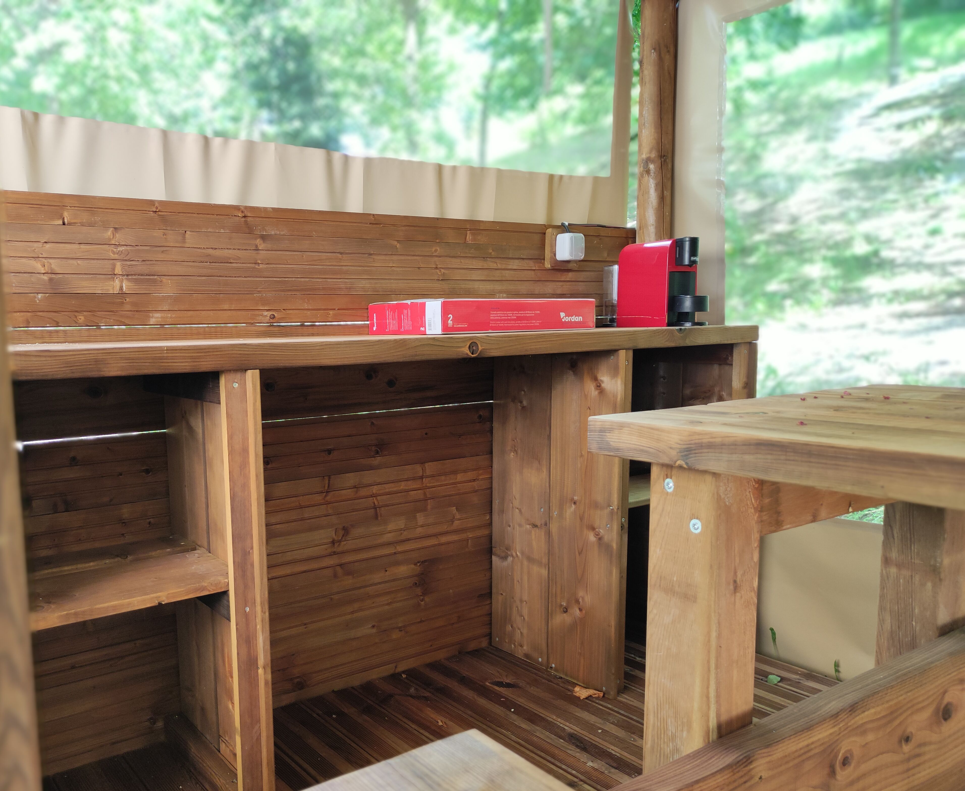 A wooden cabin interior with a wooden bench, a table, and a red box labeled "Jordan" on the wall.