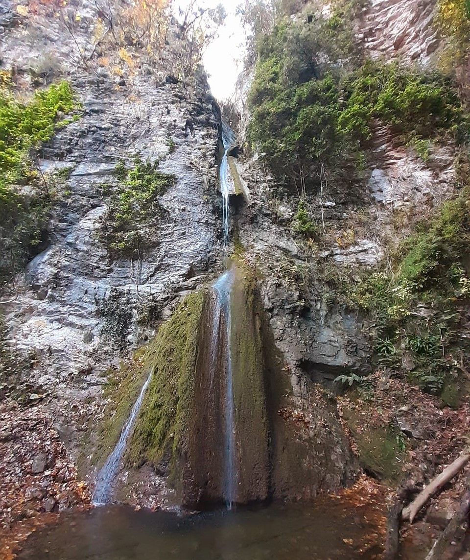Uma cascata despencando por um penhasco rochoso, rodeada por vegetação.