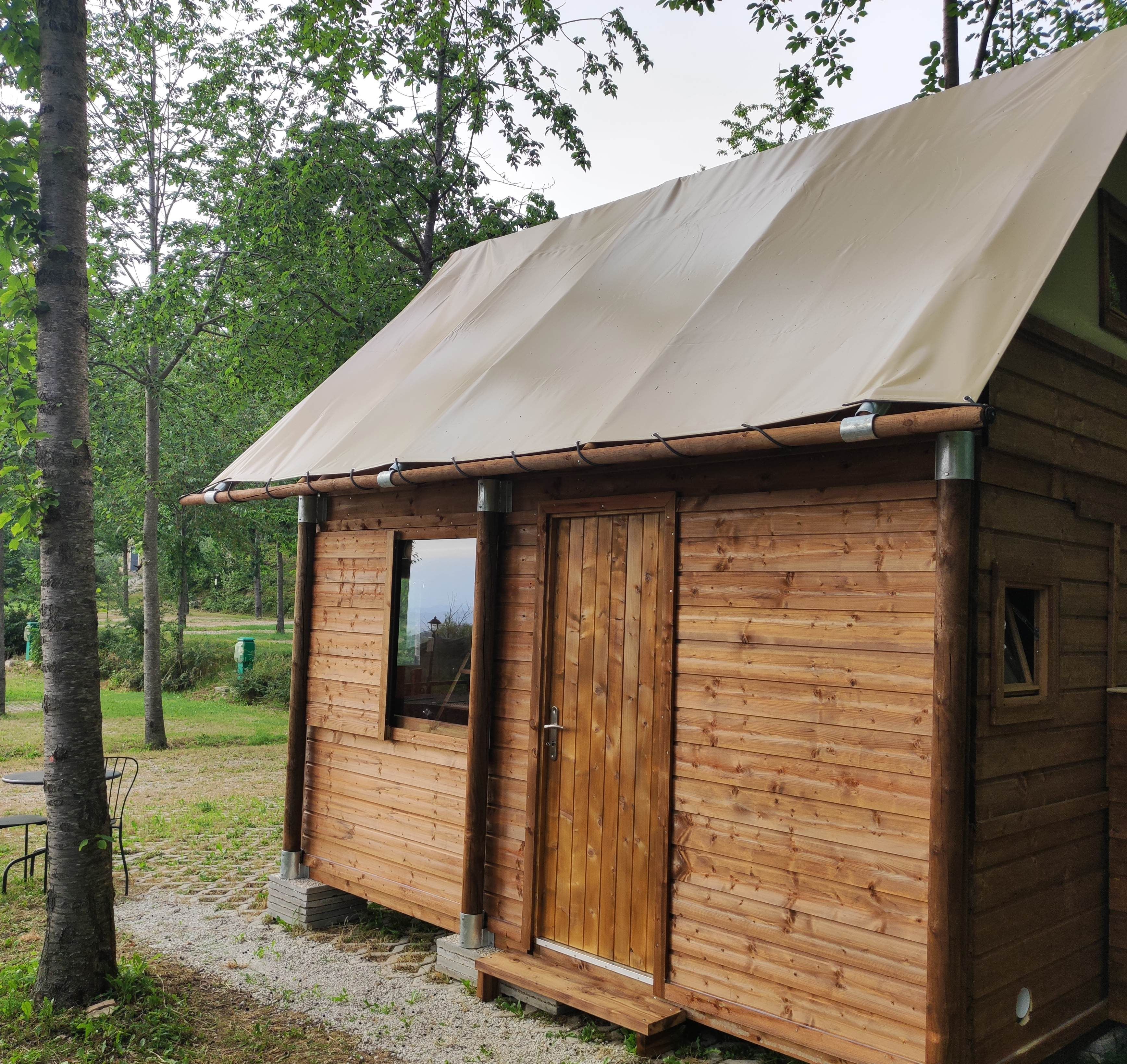 Una pequeña cabaña de madera con techo inclinado y un amplio toldo. Tiene dos puertas y una ventana.