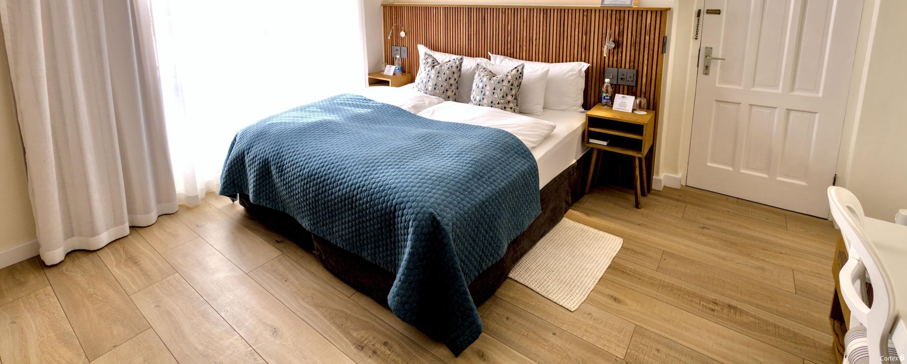 A neatly made bed with a blue blanket, wooden headboard, bedside tables with lamps, and a wooden floor.