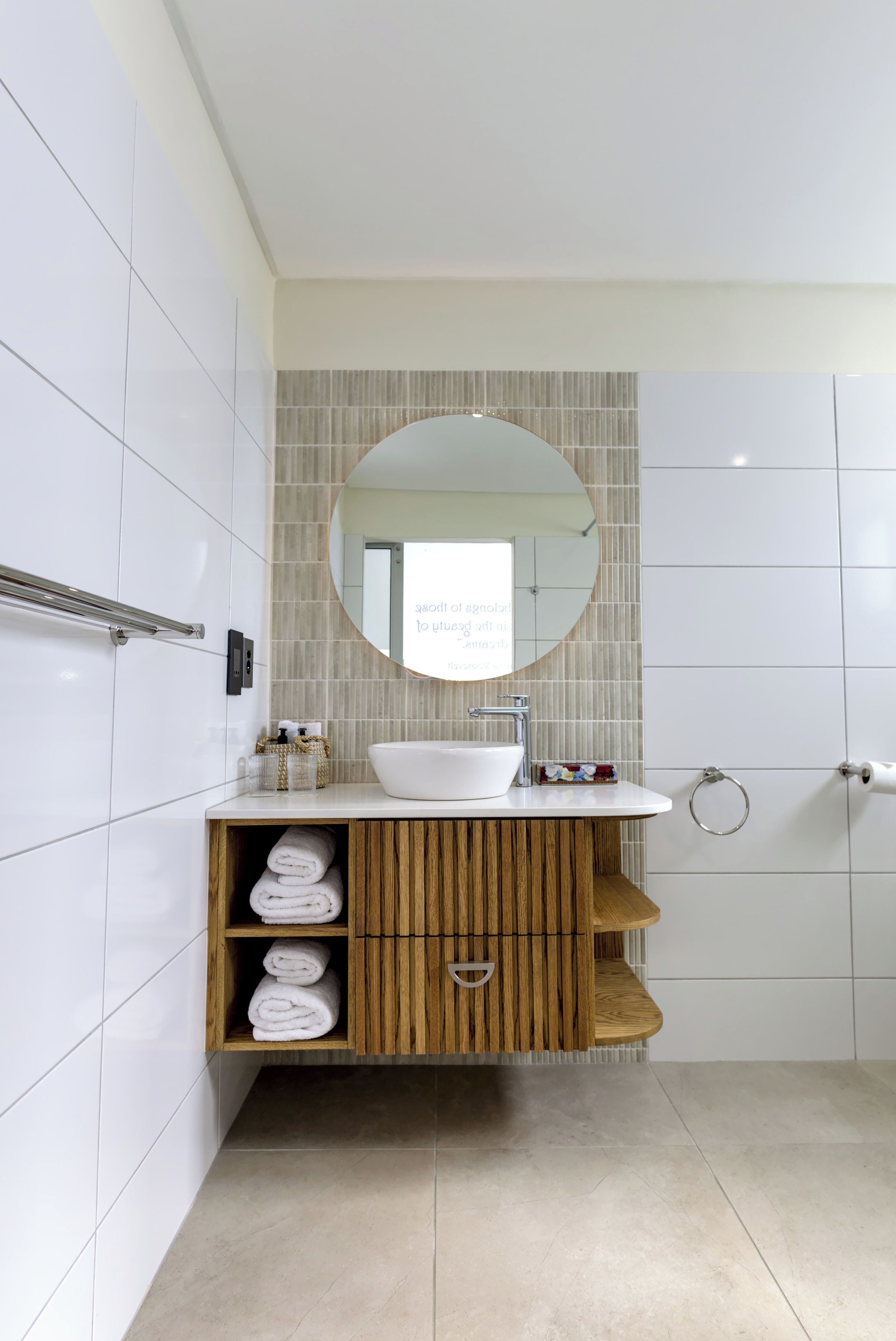 A modern bathroom with a white sink, wooden vanity, and a large mirror.