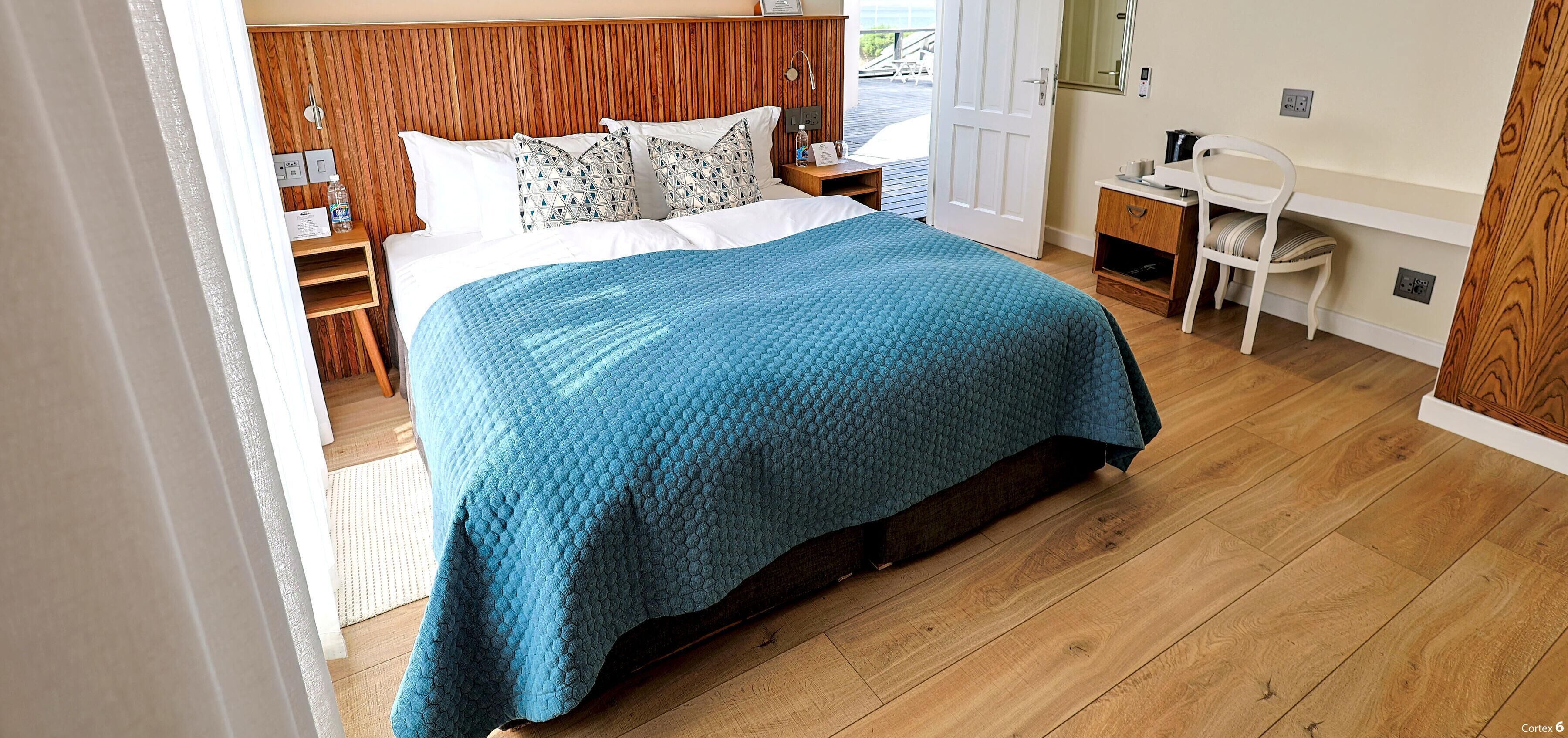 Une chambre à coucher avec une tête de lit en bois, un lit recouvert d’une couette bleue, une table de chevet avec une lampe et une chaise.