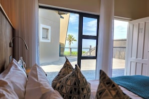 Une chambre d’hôtel avec un lit, des oreillers et une vue sur un balcon agrémenté d’un palmier et d’une terrasse en bois.