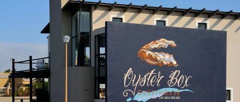 Un edificio con un gran letrero que anuncia 'Oyster Box Guesthouse', mostrando una ilustración estilizada de una ostra.