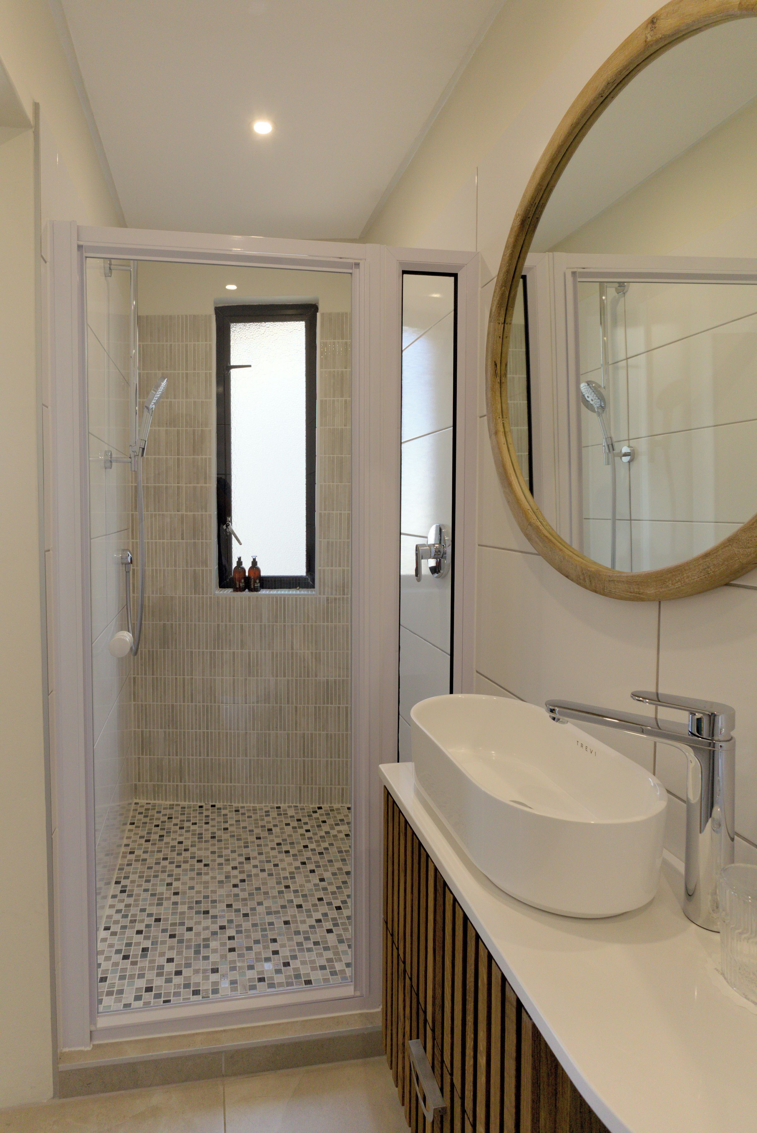 A modern bathroom with a glass-enclosed shower, a white sink, and a large mirror.