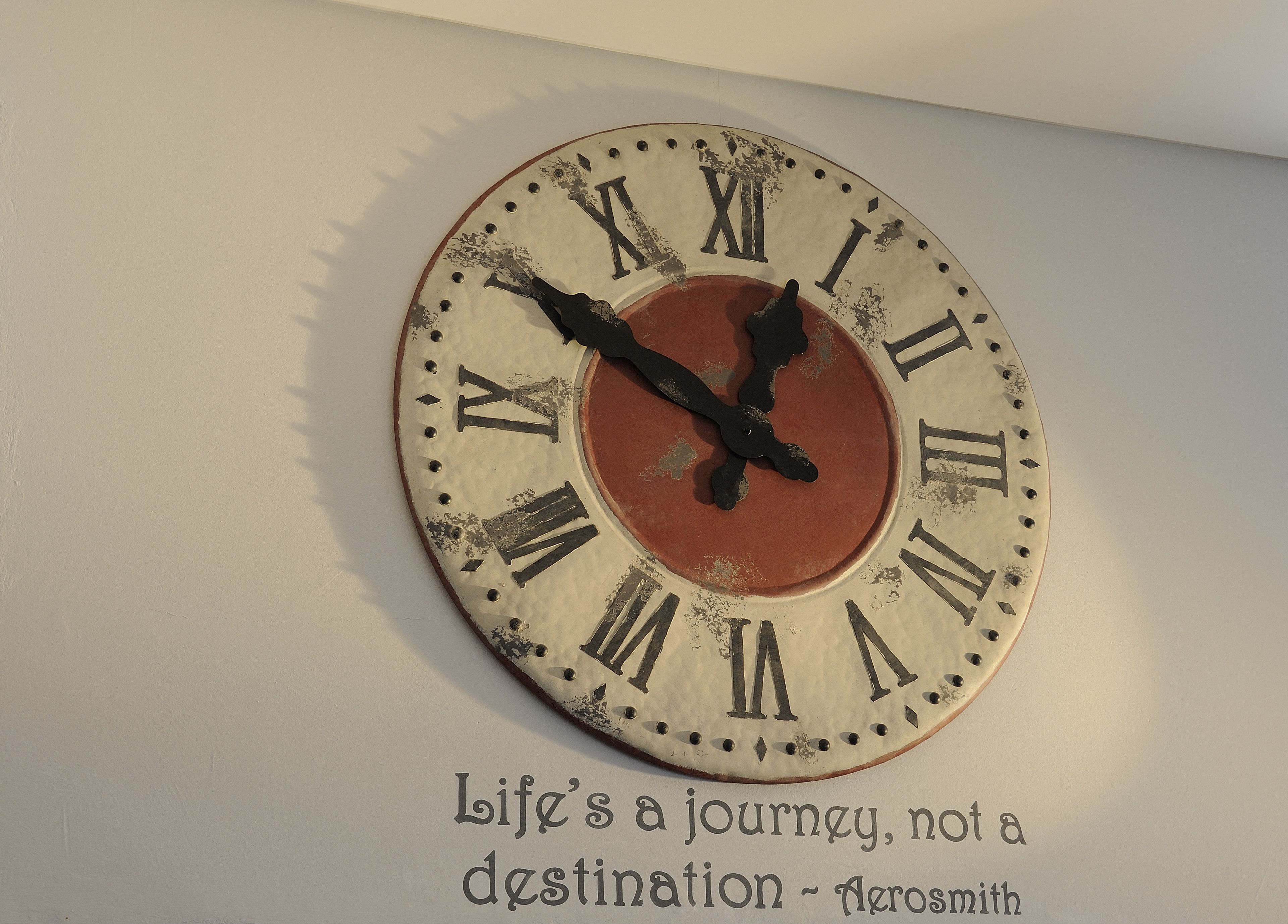 A wall clock with Roman numerals and a quote below it.