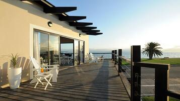 A wooden deck with white chairs and a potted plant, overlooking a body of water.