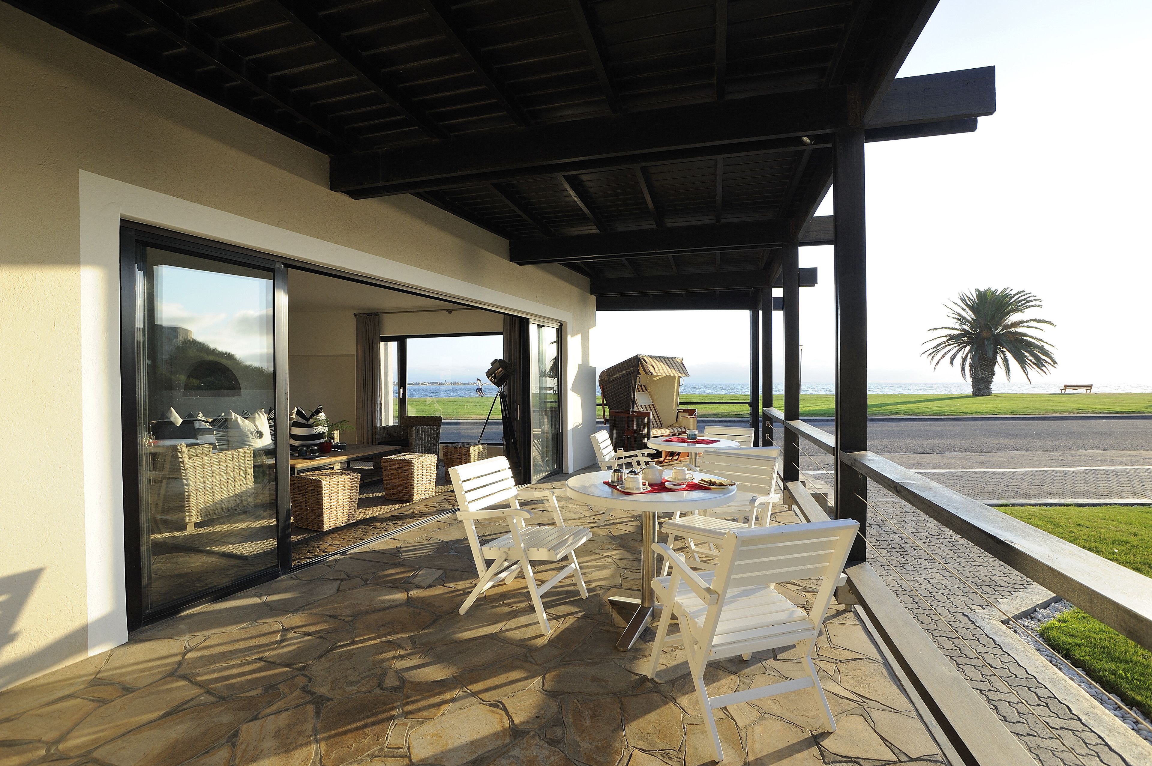 A covered patio with stone flooring, outdoor seating, and a view of the ocean.