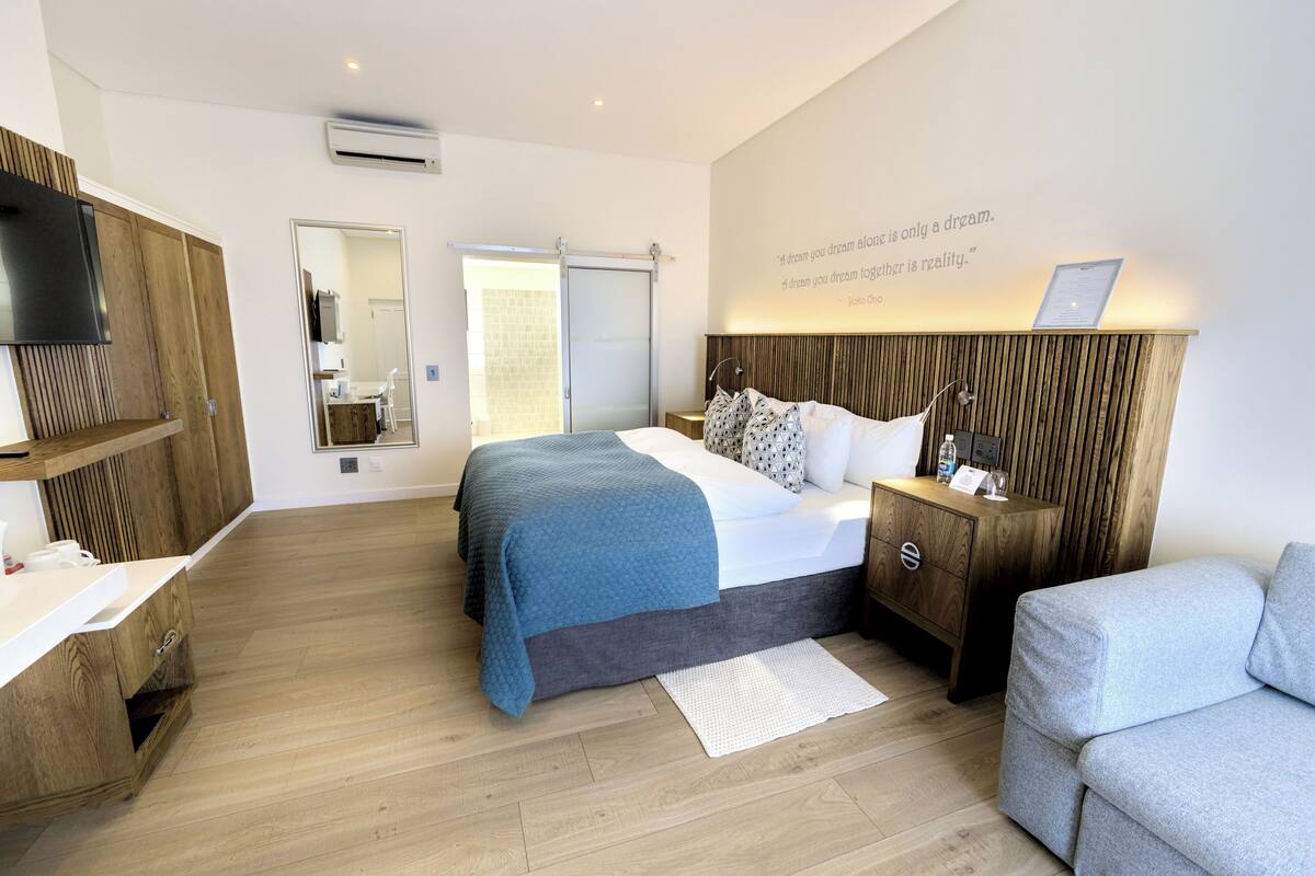 A modern hotel room with a bed, bedside table, nightstand, and a seating area.