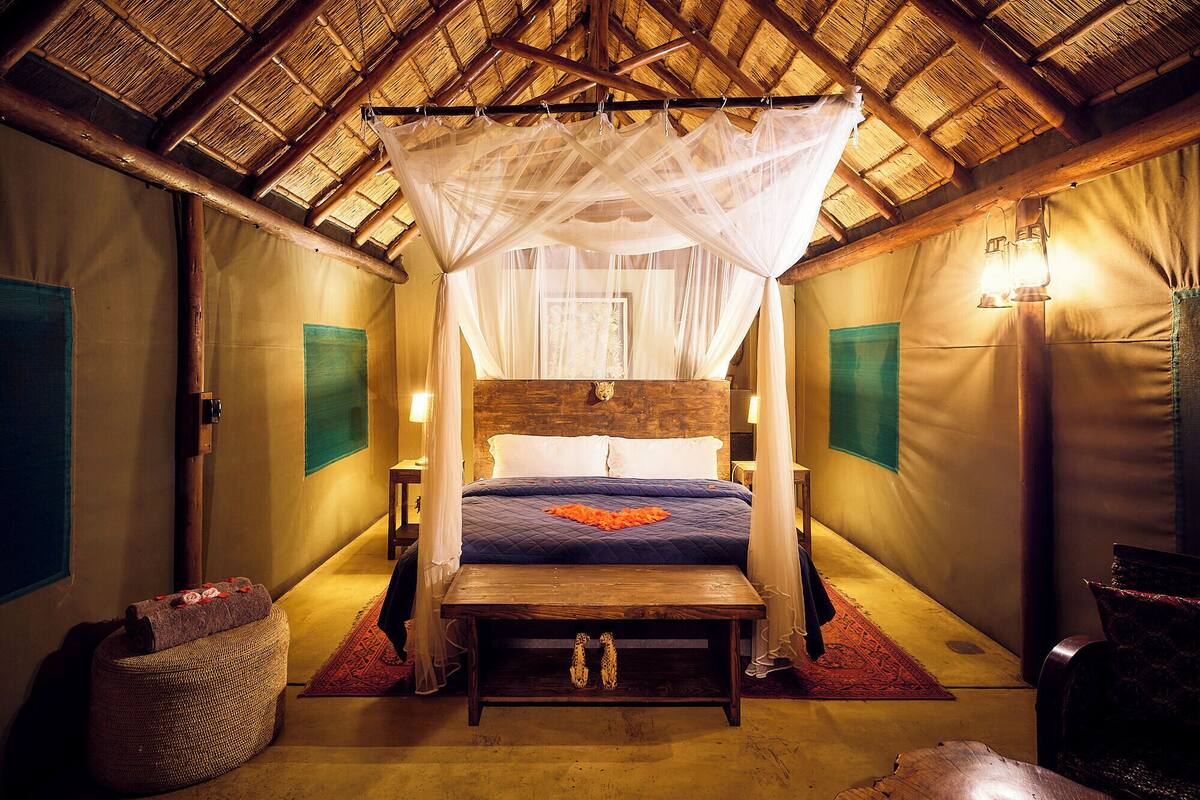 Een kamer met een bed onder een hemelbed, een houten bankje, een kleine tafel en een geweven mand.