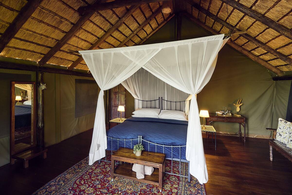 Een kamer met een hemelbed, een houten bankje, een nachtkastje en een spiegel.