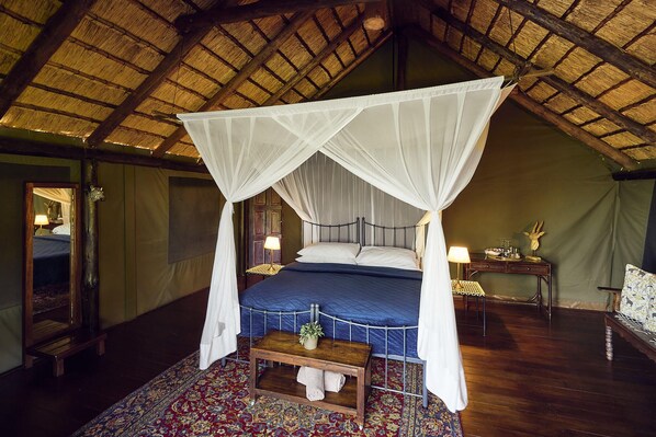 A room with a four-poster bed, a wooden bench, a nightstand, and a mirror.