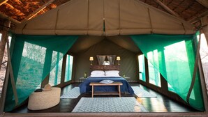 Ein Zeltraum mit Bett, Nachttischlampen, einer Bank und Blick ins Freie.