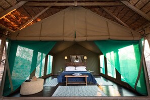 A tented room with a bed, bedside lamps, a bench, and a view of the outdoors. - Parsons Hilltop Safari Camp (Hoedspruit)