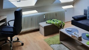 Ein modernes Loft-Apartment mit zwei Oberlichtern, einem schwarzen Bürostuhl, einer Heizung und einer gemütlichen Sitzecke mit einer Couch und Kissen.