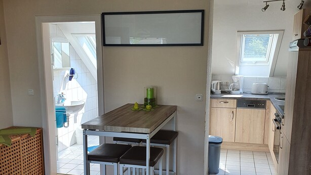 Eine moderne Küche mit Holzschränken, einem eingebauten Backofen und einem Fenster. Es gibt einen Essbereich mit Tisch und Stühlen sowie einen großen Spiegel an der Wand.