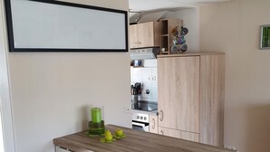Eine kleine Küche mit Holztisch und zwei Hocker, einem weißen Backofen und einem Schrank mit Küchenutensilien.