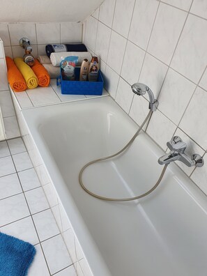 Een bad/douchecombinatie, een haardroger, handdoeken, zeep