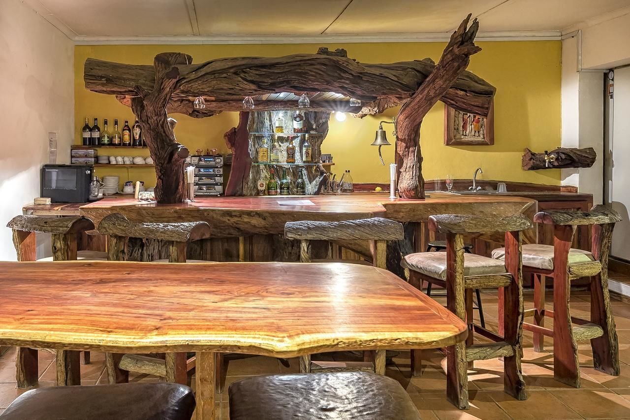 A rustic bar area with wooden furniture and a shelf of bottles.