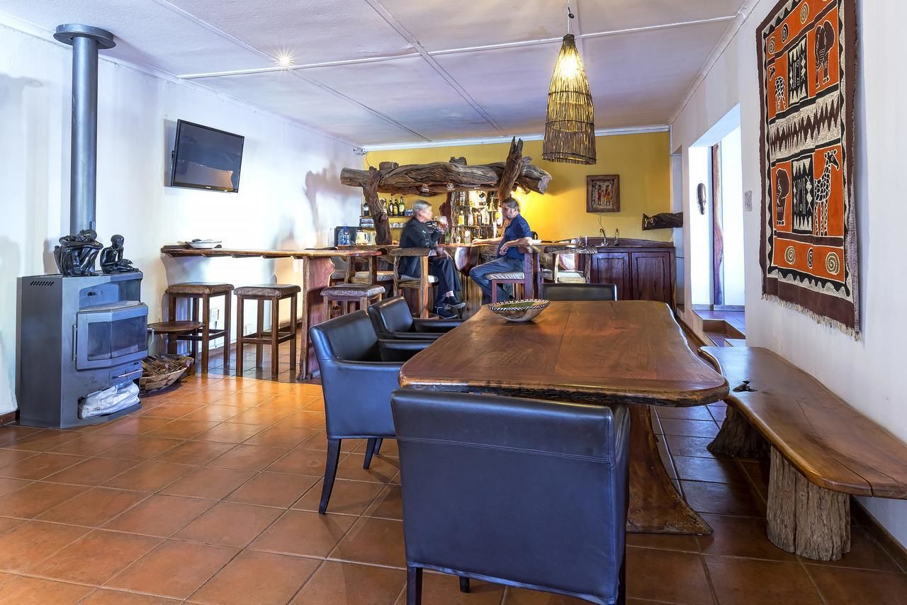 Un rincón de bar acogedor con una larga mesa de madera, varias sillas y un televisor montado en la pared.