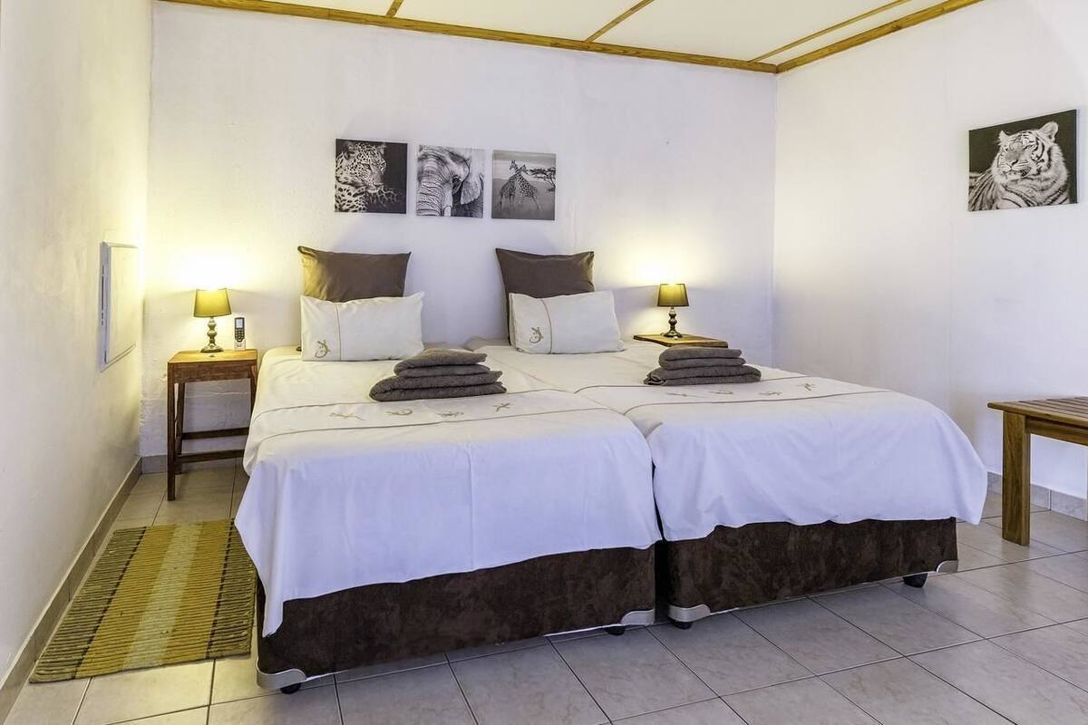 A double bed with white linens and two pillows, a bedside table with a lamp, and a wall-mounted artwork of a tiger.
