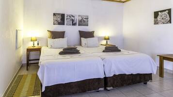 Una cama doble con sábanas blancas y dos almohadas, una mesita de noche con lámpara, y una obra de arte colgada en la pared con un tigre.