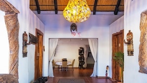 A hallway with a thatched roof, a hanging chandelier, and a mat with the hotel name. - Trans Kalahari Inn (Windhoek)