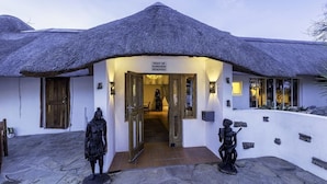 A building with a thatched roof entrance, a sign indicating 'Right of Admission Reserved', and two statues on the ground. - Trans Kalahari Inn (Windhoek)