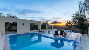 A modern outdoor pool area with a clear view of the sunset, surrounded by lounge chairs and a patio table. - Trans Kalahari Inn (Windhoek)