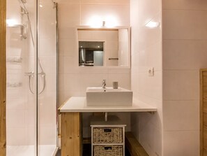 A modern bathroom with a glass shower enclosure, a white sink with a mirror above, and a wooden cabinet below.