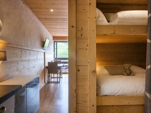 Un interior de madera con una litera, un escritorio con silla y un televisor.