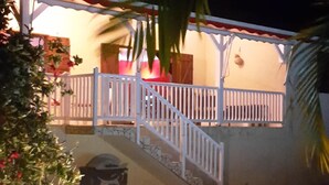 A nighttime view of a house with a swimming pool, a staircase leading to a porch, and a white railing. - Creole villa with pool in tropical garden   (Sainte Rose)