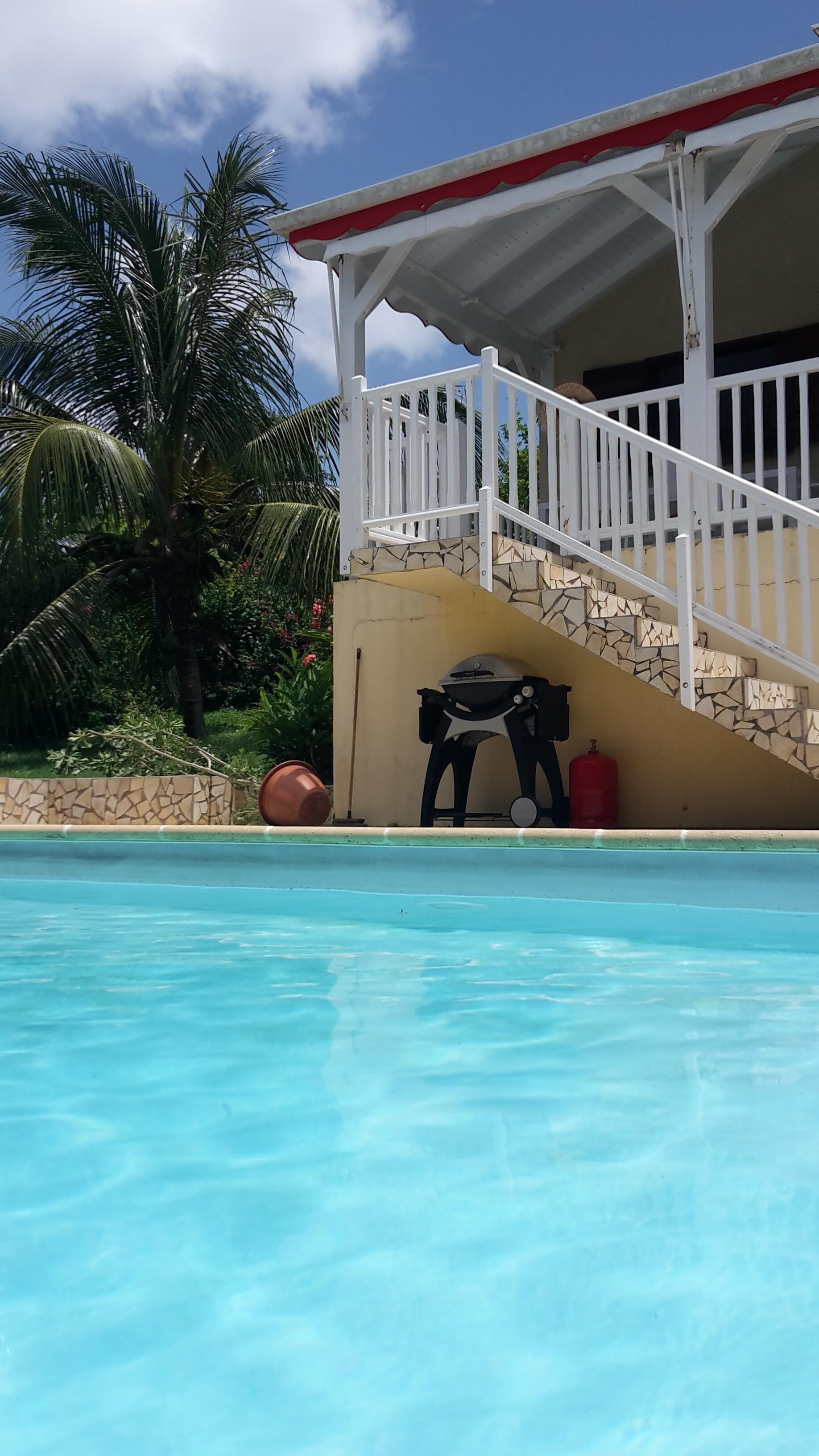 Un área de piscina con barandilla blanca, una escalera de piedra y una parrilla.