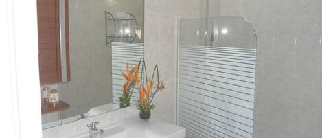 A bathroom with a white sink, a mirror, a shower enclosure, and a potted plant with orange flowers.