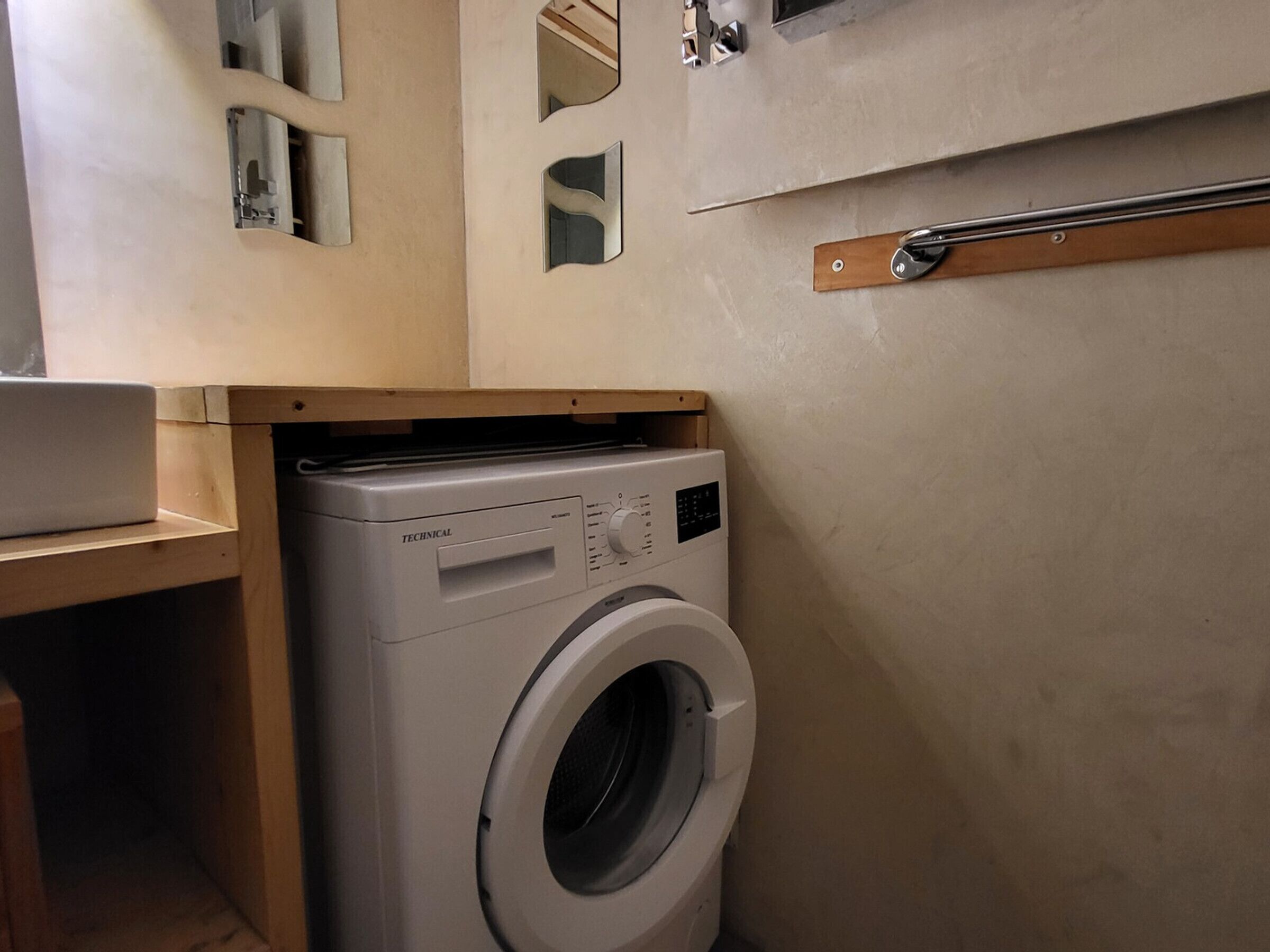 A compact laundry room with a front-loading washing machine, wooden cabinets, and a towel rack.