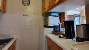 A compact kitchen with white tiled walls, wooden cabinets, a microwave, a coffee maker, and a kettle on the counter. - Tignes: 2-room apartment 41m², 500m from slopes, southwest balcony, wifi, 4-5 pers. (Tignes)