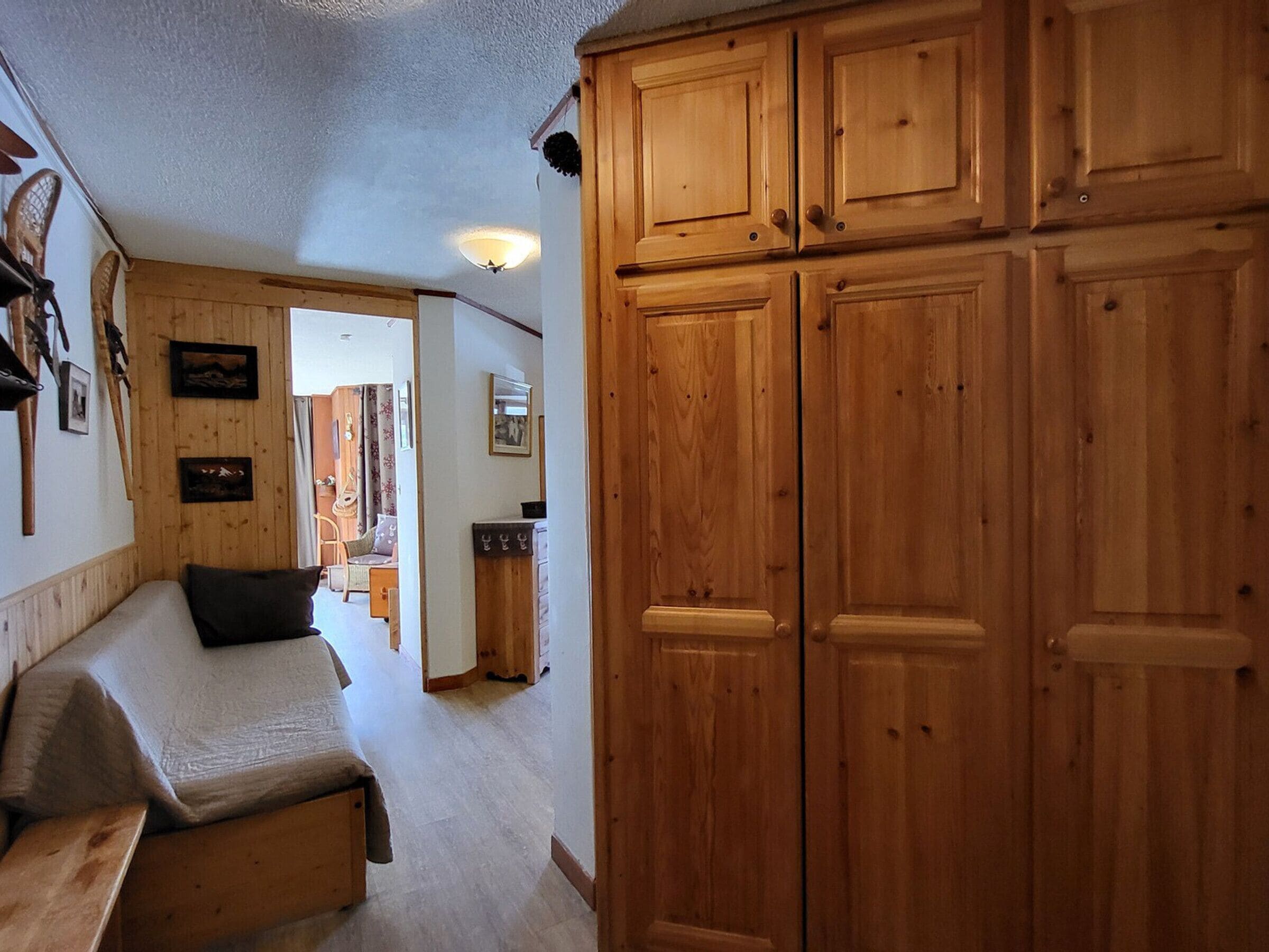 A room with a bed, wooden wardrobe, and a desk with a chair.