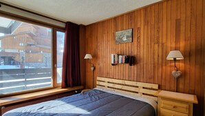 A bedroom with a wooden paneled wall, a bed with a blue quilt, a bedside table with a lamp, and a bookshelf. - Tignes: 2-room apartment 41m², 500m from slopes, southwest balcony, wifi, 4-5 pers. (Tignes)