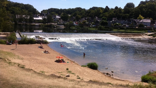 Ein Flussufer mit einem Strand, an dem Menschen entspannen und schwimmen.