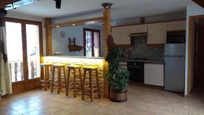 Una cocina con una isla central, taburetes de madera, una planta en maceta y un refrigerador.