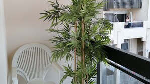 Un balcon orné d’un pot de bambou, d’une chaise en plastique blanche et offrant une vue sur un immeuble doté de balcons.